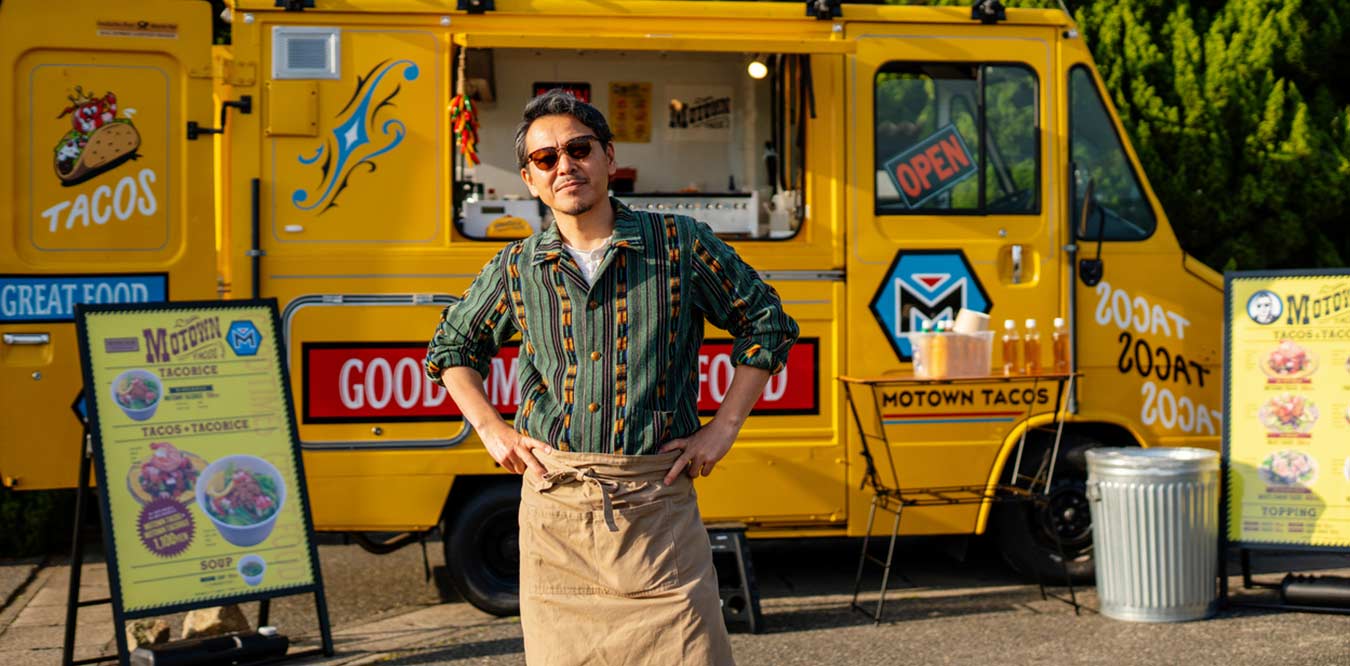 a male entrepreneur standing in front of his yellow food truck